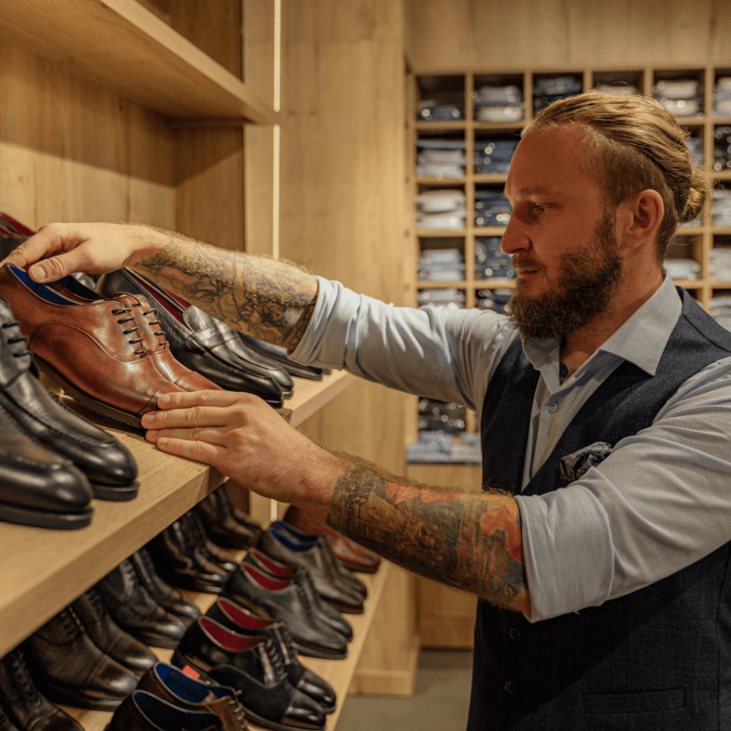 Retail worker organizing sustainable men's shoes on store shelves, showcasing eco-friendly and stylish footwear options.