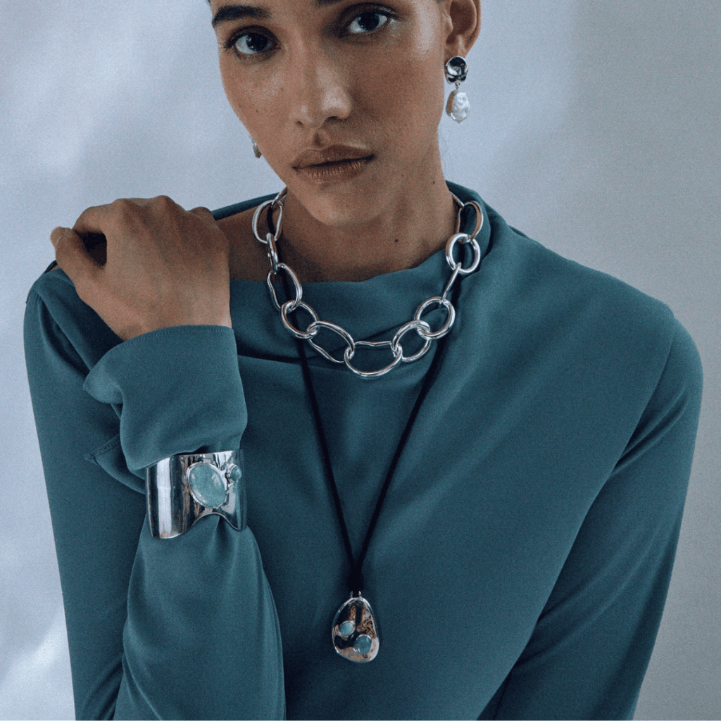 Woman wearing Lizzie Fortunato ethical jewelry, including silver chain necklace, pearl earrings, and statement cuff, all crafted with sustainability in mind.